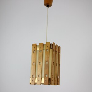 Könnte beinhalten: Eine Holz-Pendelleuchte mit einem weißen Stoffschirm. Die Leuchte hat eine rechteckige Form und besteht aus dünnen Holzlatten mit Messingakzenten.