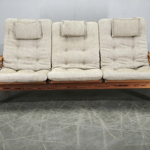 May include: A three-seater sofa featuring a natural light wood frame and beige textured fabric cushions. The backrest includes three integrated headrests and button-tufted detailing across the seat and back cushions, showcasing a visible wood grain.