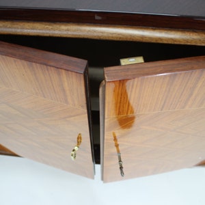 May include: Two wooden cabinet doors with a geometric pattern are open, revealing the interior of the cabinet. The doors have brass handles and are finished in a dark wood stain.