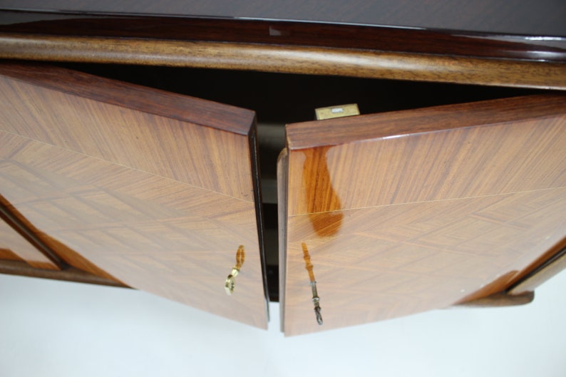 May include: Two wooden cabinet doors with a geometric pattern are open, revealing the interior of the cabinet. The doors have brass handles and are finished in a dark wood stain.