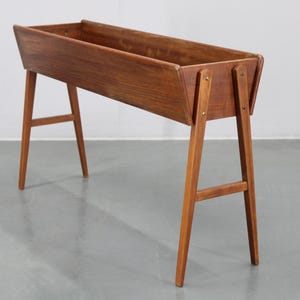 May include: A wooden planter stand with a rectangular planter box and four legs. The planter is made of dark wood and has a natural finish.