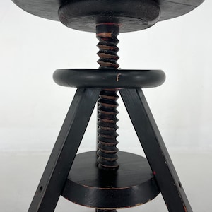 May include: Black wooden adjustable stool with a round seat and three legs. The stool has a threaded screw mechanism for height adjustment.