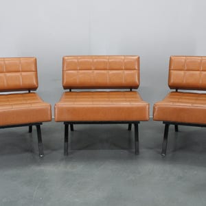 May include: Three brown leather chairs with black metal frames. The chairs have a tufted design on the back and seat.