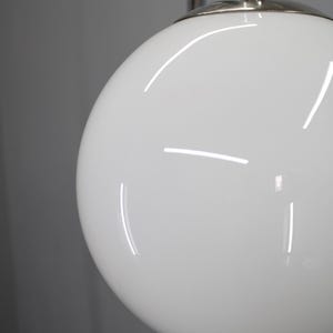 May include: Close-up of a white, spherical lamp shade with a glossy finish. The shade is part of a chrome and silver floor lamp. The lamp is against a gray background.