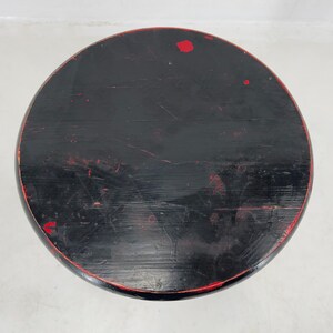 May include: Black wooden stool with red paint accents. The stool has a round top and a simple design.