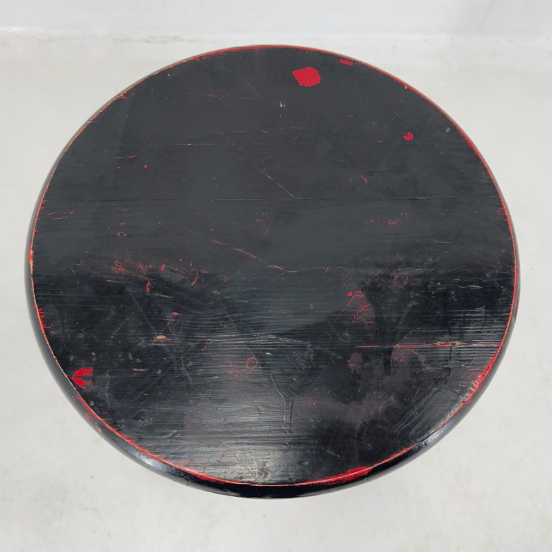 May include: Black wooden stool with red paint accents. The stool has a round top and a simple design.