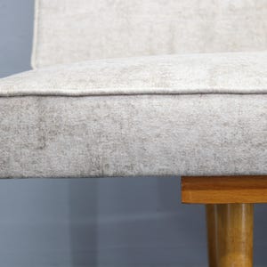 May include: A close-up of a light gray fabric sofa with wooden legs. The sofa has a simple, modern design.