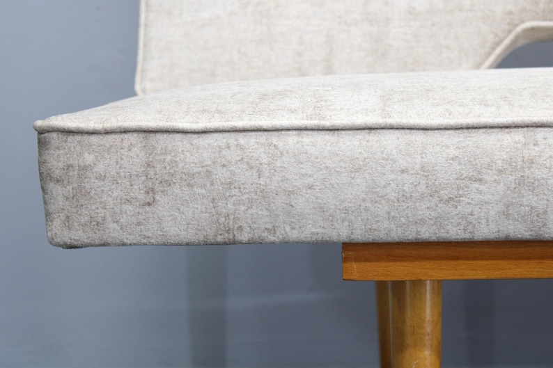 May include: A close-up of a light gray fabric sofa with wooden legs. The sofa has a simple, modern design.