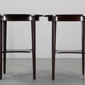 Può includere: Due tavolini rotondi marrone scuro con gambe sottili. Ogni tavolo ha un ripiano inferiore e un design minimalista. I tavoli sono in legno e sono posti su uno sfondo neutro. Misurano circa 60 cm di altezza.