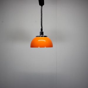 May include: An orange pendant light with a chrome base and a black, coiled cord. The light fixture has a rounded, dome-shaped shade. The light is suspended from the ceiling.