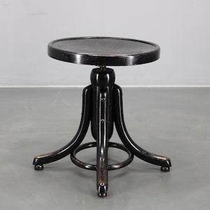 Puede incluir: Un taburete negro ajustable con asiento redondo. El taburete tiene un diseño de patas curvas y un reposapiés circular. El asiento tiene aproximadamente 30 cm de diámetro.