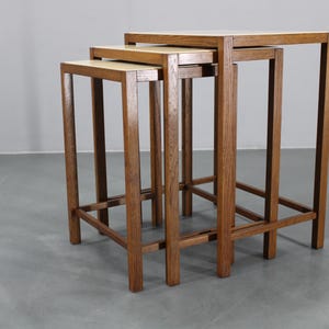 May include: Set of three nesting tables with a light wood finish. The tables have a rectangular top and a square leg design. The largest table is approximately 24 inches tall, the medium table is 20 inches tall, and the smallest table is 16 inches tall.