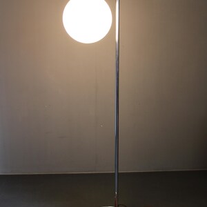 May include: A modern floor lamp with a chrome finish and a spherical white glass shade. The lamp has a curved arm and a round base with a wood grain pattern. The lamp's height is approximately 60 inches.
