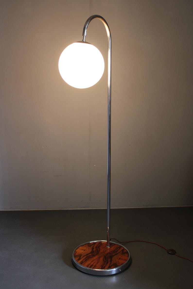 May include: A modern floor lamp with a chrome finish and a spherical white glass shade. The lamp has a curved arm and a round base with a wood grain pattern. The lamp's height is approximately 60 inches.