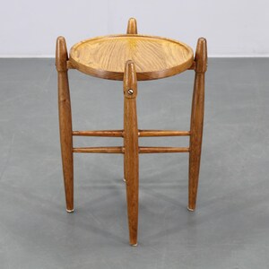 Peut inclure: Petite table d'appoint ronde en bois clair, avec trois pieds et un plateau circulaire. Le bois est de couleur marron clair et présente un design simple et minimaliste. Les pieds sont légèrement effilés.