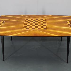 Op de afbeelding: Een houten tafel met een schaakbordinleg in het midden. De tafel heeft een zwart metalen frame en vier poten.