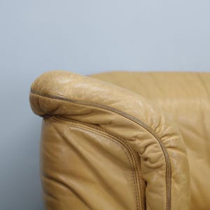 May include: Close-up of a tan leather armchair with a tufted back and rolled arms.