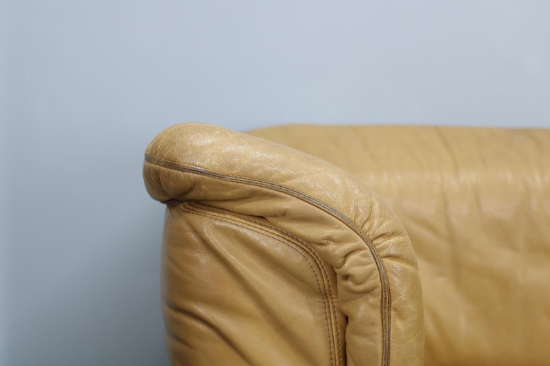 May include: Close-up of a tan leather armchair with a tufted back and rolled arms.