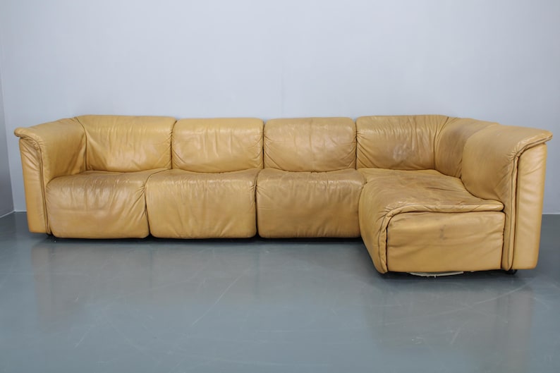 May include: A large, tan leather sectional sofa with a chaise lounge. The sofa is made up of four separate pieces that can be arranged in different configurations.