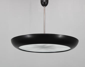 May include: A contemporary black circular pendant light. The light features a wide, shallow shade with a white interior and a black exterior. It is suspended from the ceiling by a thin, silver rod and a black canopy.