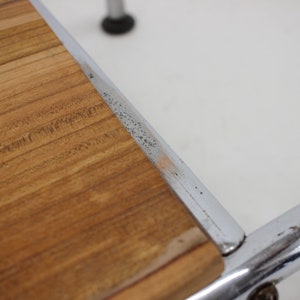 May include: Close-up of a wooden top surface of a chrome and wood stool. The wood is a light brown color and has a natural grain pattern. The chrome frame is visible around the edge of the wood top.