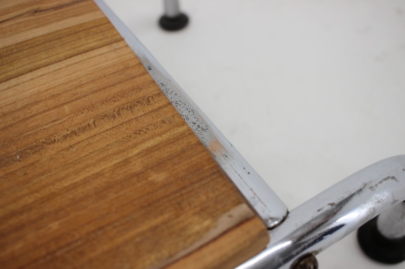 May include: Close-up of a wooden top surface of a chrome and wood stool. The wood is a light brown color and has a natural grain pattern. The chrome frame is visible around the edge of the wood top.