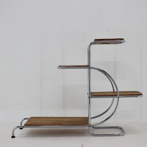 May include: A chrome and wood plant stand with four shelves. The stand has a curved design and is made of polished chrome metal with wooden shelves.