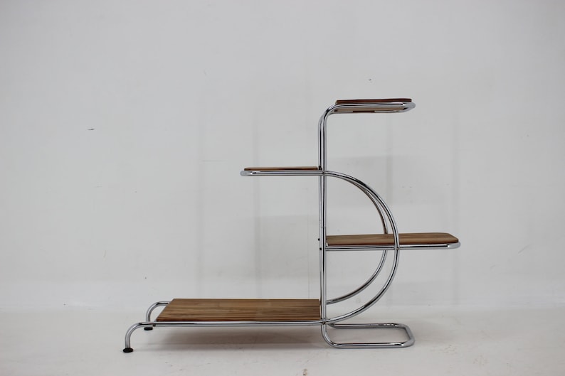May include: A chrome and wood plant stand with four shelves. The stand has a curved design and is made of polished chrome metal with wooden shelves.