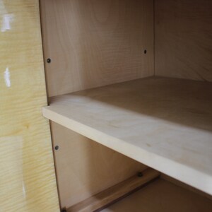 May include: Inside view of a wooden cabinet with a light wood finish. The cabinet has one shelf and is empty.