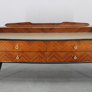 Può includere: Comò moderno di metà secolo con motivo a spina di pesce sui frontali dei cassetti. Il comò ha quattro cassetti con maniglie ad anello dorate, un piano in vetro e gambe affusolate con dettagli dorati. Il legno è di colore marrone caldo.