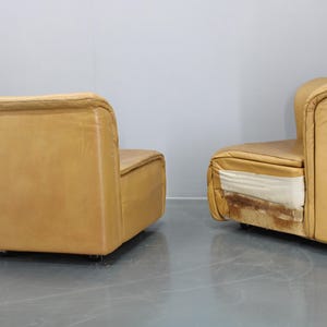 May include: Two tan leather modular sofas with a modern design. The sofas are in a showroom setting with a white wall in the background.