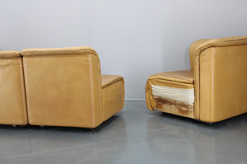 May include: Two tan leather modular sofas with a modern design. The sofas are in a showroom setting with a white wall in the background.