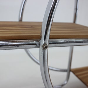 May include: Close-up of a chrome shelf unit with two wooden shelves. The shelves are supported by curved chrome rods. A screw is visible on the side of the shelf.