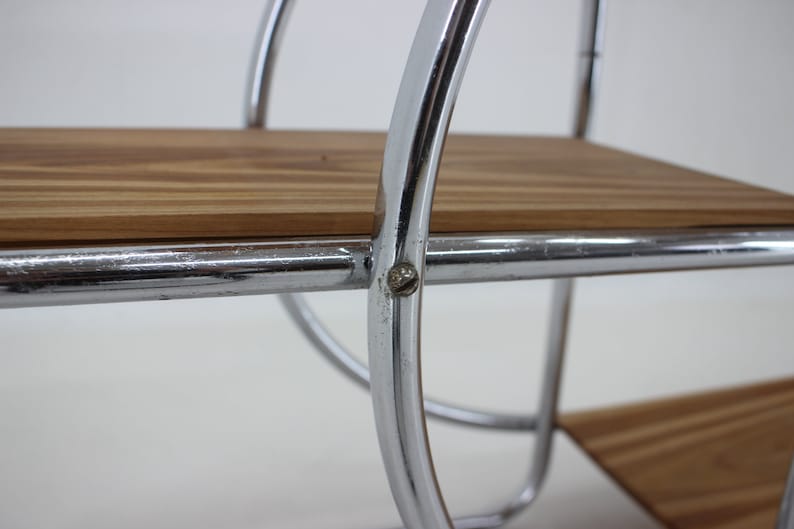 May include: Close-up of a chrome shelf unit with two wooden shelves. The shelves are supported by curved chrome rods. A screw is visible on the side of the shelf.