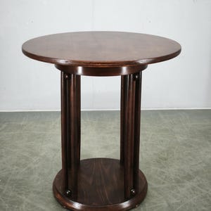 May include: A round dark brown wooden pedestal table featuring a smooth circular top supported by four vertical cylindrical columns that connect to a matching circular base, creating a stable structure with a consistent wood grain finish.