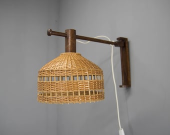May include: A wall-mounted light fixture with a brown wooden arm and a woven wicker shade. The shade is round and has a light brown color.