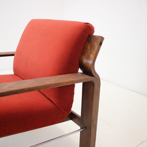 May include: A mid-century modern armchair with a vibrant red cushion and dark wood frame. The chair features a curved backrest and armrests, with a sleek, minimalist design. The frame is made of dark wood, and the cushion is a solid red color.