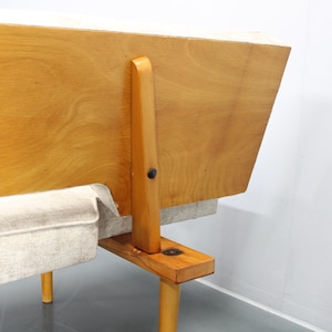 May include: A wooden frame sofa with a light gray fabric cushion. The sofa has a simple design with a wooden frame and legs.