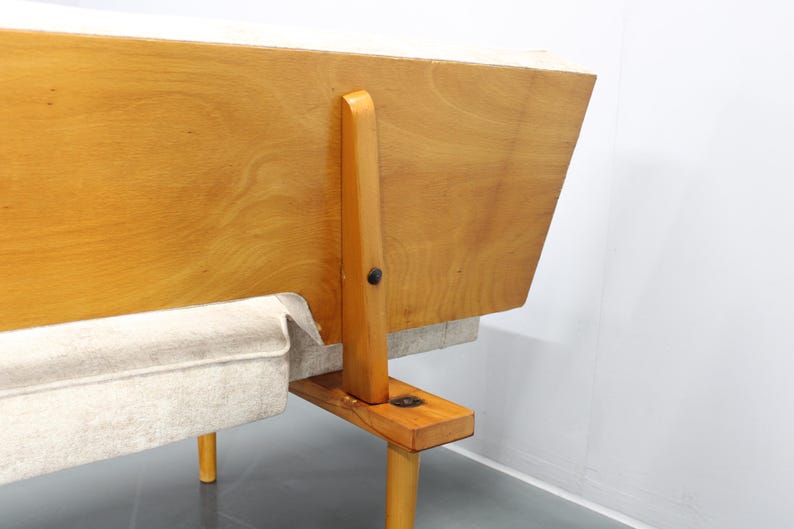 May include: A wooden frame sofa with a light gray fabric cushion. The sofa has a simple design with a wooden frame and legs.