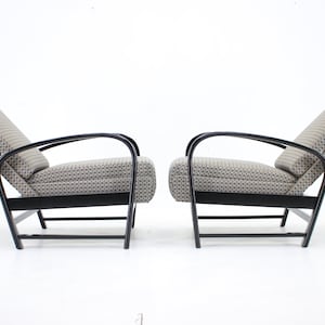 May include: A pair of mid-century lounge chairs. They feature black metal frames and patterned, light grey and beige upholstery. The chairs are designed for reclining, with angled backs.