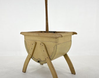 May include: A vintage wooden laundry tub with a light yellow paint finish and a wooden handle. The tub has a rounded bottom and four legs.