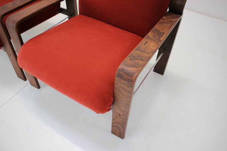 May include: Close-up of a mid-century modern chair with a vibrant orange seat and dark wood frame. The chair features a curved armrest and sturdy legs, showcasing a blend of comfort and style. The design is reminiscent of classic furniture.