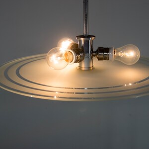 May include: A chrome ceiling light fixture with a frosted glass shade featuring concentric circles. The light fixture has three exposed light bulbs.