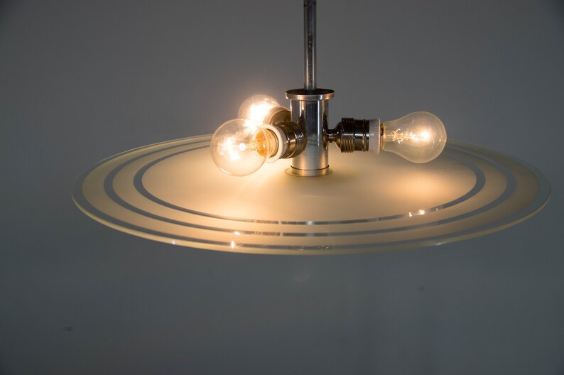May include: A chrome ceiling light fixture with a frosted glass shade featuring concentric circles. The light fixture has three exposed light bulbs.