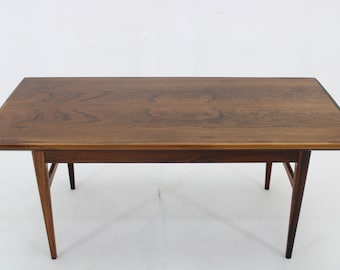 May include: A rectangular wooden coffee table with a dark brown finish. The table has a simple design with four angled legs and a lower shelf. The tabletop is approximately 48 inches long and 24 inches wide.