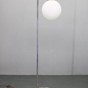 May include: A modern floor lamp with a chrome finish and a white globe shade. The lamp has a curved arm and a round base with a wood grain pattern. The lamp's height is approximately 60 inches.