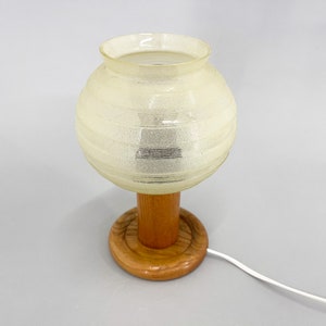 Puede incluir: Una l&aacute;mpara de mesa vintage con una pantalla de vidrio blanco esmerilado y una base de madera. La pantalla tiene un dise&ntilde;o texturizado y acanalado.