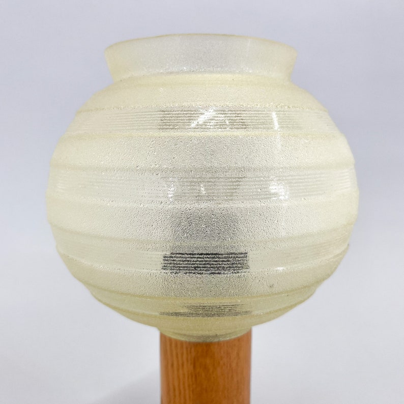 Puede incluir: Una pantalla de l&aacute;mpara de vidrio blanco esmerilado con l&iacute;neas horizontales y una base de madera.