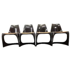Könnte beinhalten: Vier schwarze Stühle mit geschwungenem Design. Die Stühle haben eine glänzende Oberfläche und eine hellfarbige Sitzfläche. Die Stühle haben ein einzigartiges, offenes Rahmendesign mit geschwungenem Sockel und Rücken.