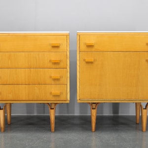 Op de afbeelding: Twee houten dressoirs, een met vier lades en de andere met één lade. Beide dressoirs hebben een lichte houtkleur en staan op vier poten.